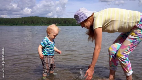 Mom and her little son play and splash around in the clear water of a forest lake on a sunny summer day against a blue sky