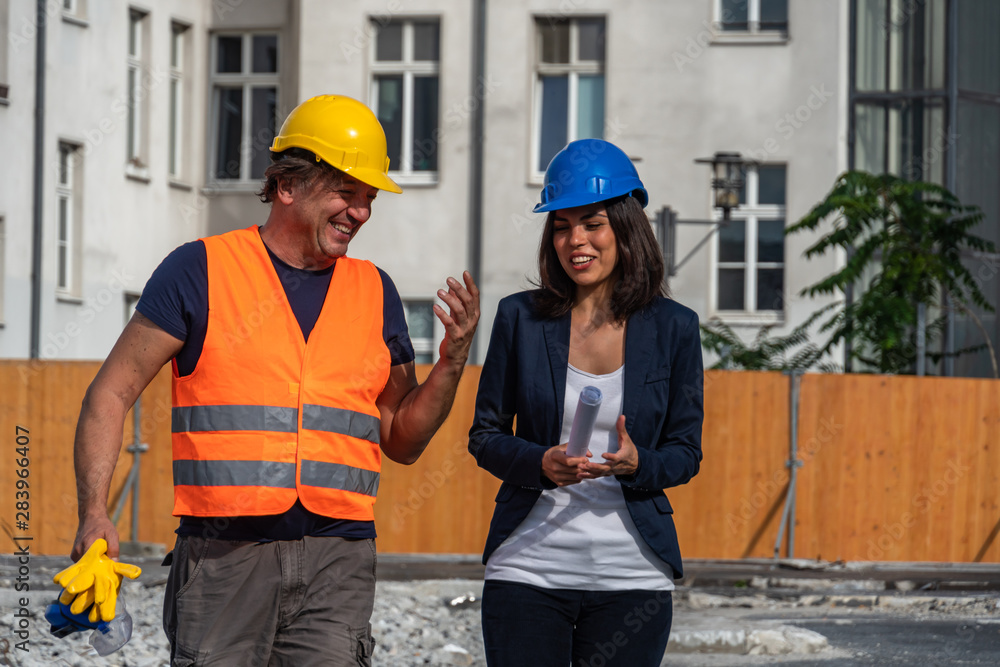 Two civil engineers, a man and a brunette young woman, talking and laughing during the work break. Outdoors
