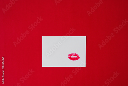 Red lipstick lip print Kiss on white paper sheet on red background © Sunshine
