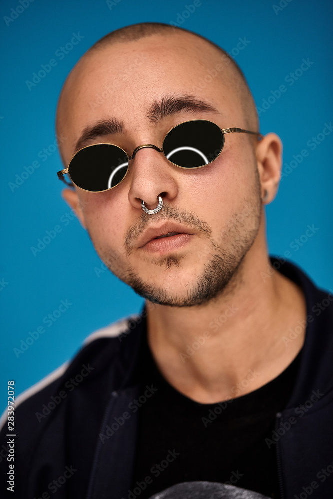 Studio shot of a young tattoed bald man posing against a blue background. 90s style. Studio shot of a young tattoed bald man posing against a blue background. 90s style.