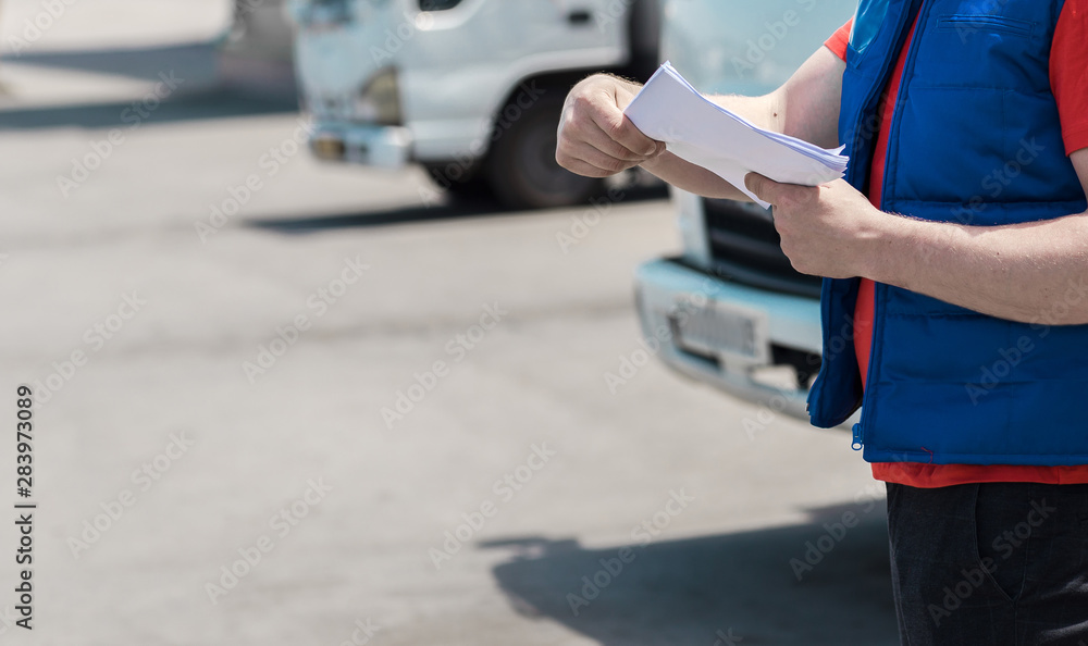 Fototapeta premium Courier driver in uniform making notes in document and delivery white truck behinde him