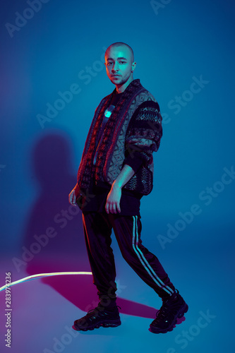 Studio shot of a young tattoed bald man posing against a colorful background. 90s style. © nazarovsergey