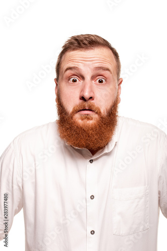 Portrait of a young, chubby, redheaded man in a white shirt making faces at the camera, isolated on a white background