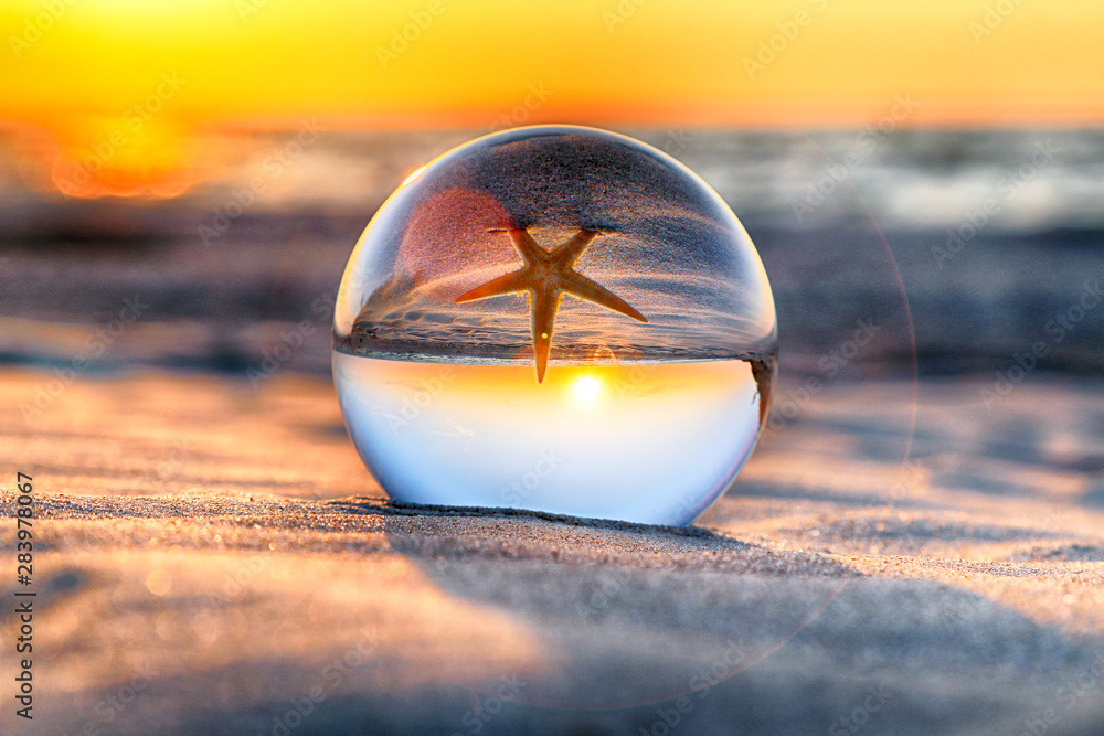 Beautiful sunset on the beach in Slowinski National Park near Leba, Poland.  View of a starfish through a glass, crystal ball (lensball) for refraction  photography. Wild, untouched nature. Stock Photo
