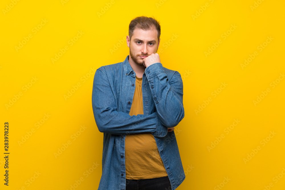 Fototapeta premium Blonde man over isolated yellow wall having doubts