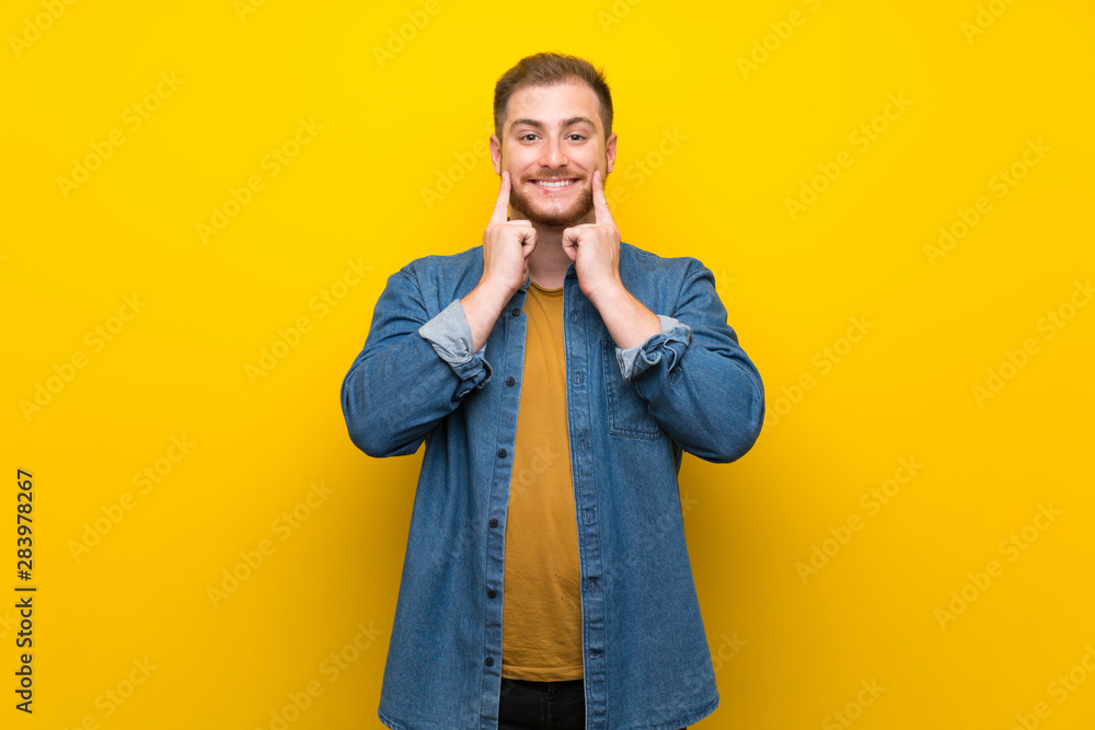 Blonde man over isolated yellow wall smiling with a happy and pleasant expression Blonde man over isolated yellow wall smiling with a happy and pleasant expression