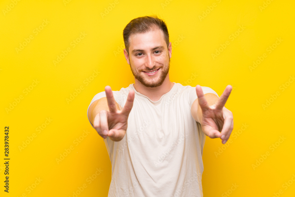 Handsome man over yellow background smiling and showing victory sign Handsome man over yellow background smiling and showing victory sign