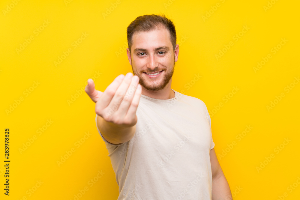 Handsome man over yellow background inviting to come Handsome man over yellow background inviting to come