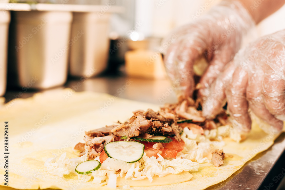 partial view of cook in gloves preparing doner kebab