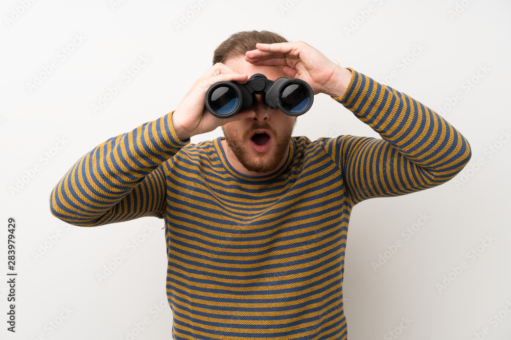 Handsome man over isolated white wall with black binoculars Handsome man over isolated white wall with black binoculars