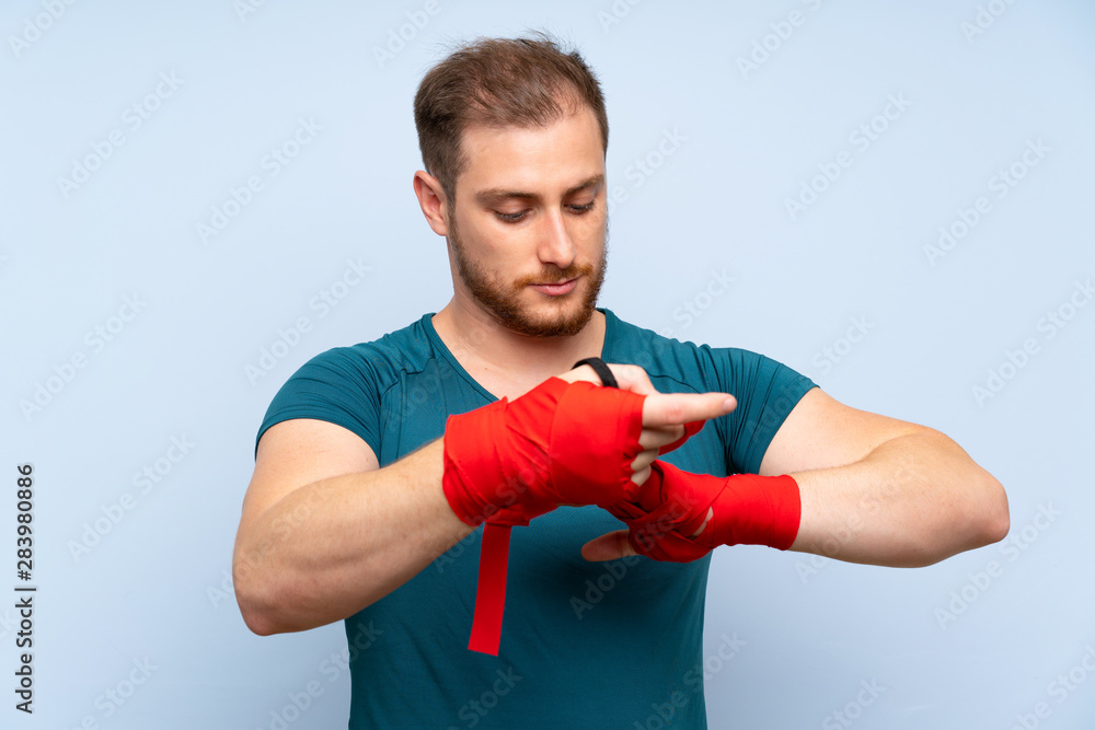 Blonde sport man over blue wall in boxing bandages Blonde sport man over blue wall in boxing bandages