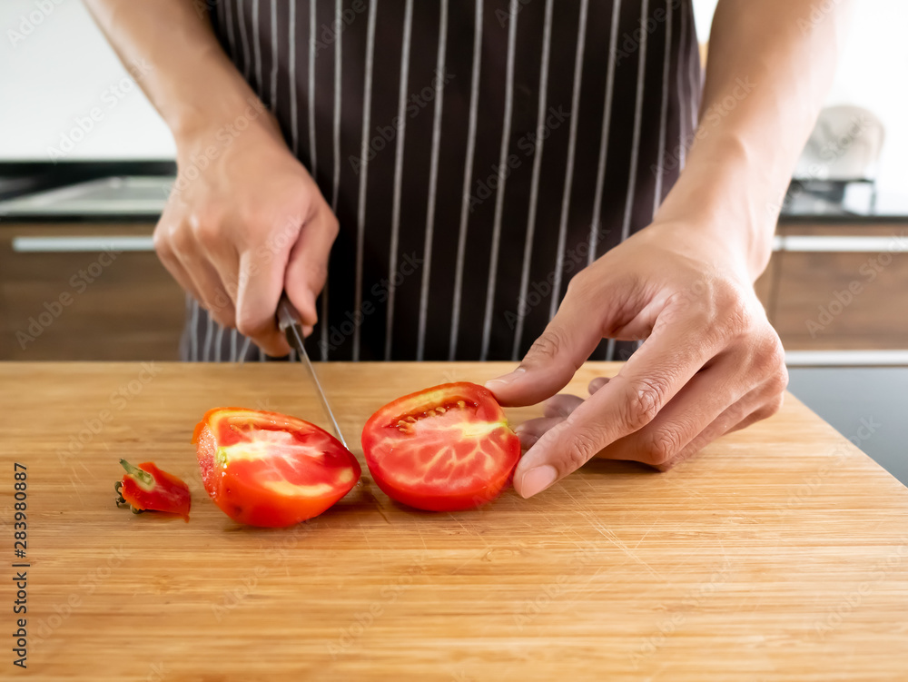 Asian chef man chopping fresh organic red tomato on wooden chopping board by sharpen knife in the kitchen for cooking diet healthy food Asian chef man chopping fresh organic red tomato on wooden chopping board by sharpen knife in the kitchen for cooking diet healthy food
