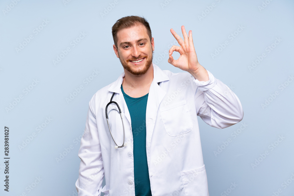 Handsome doctor man over blue wall showing ok sign with fingers Handsome doctor man over blue wall showing ok sign with fingers