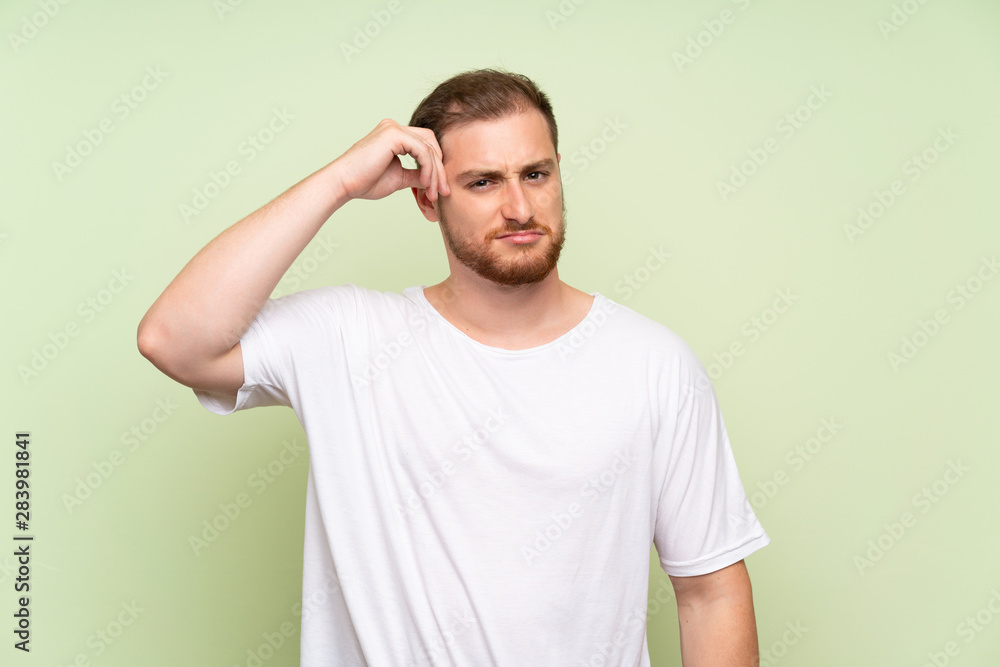 Fototapeta premium Handsome man over green background having doubts and with confuse face expression