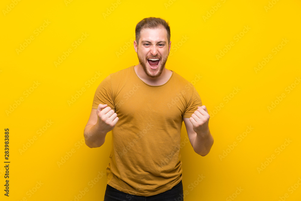 Blonde man over isolated yellow wall frustrated by a bad situation Blonde man over isolated yellow wall frustrated by a bad situation