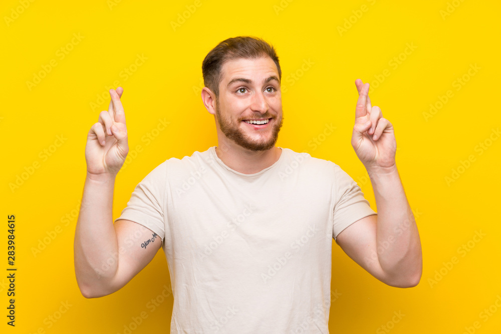 Handsome man over yellow background with fingers crossing Handsome man over yellow background with fingers crossing