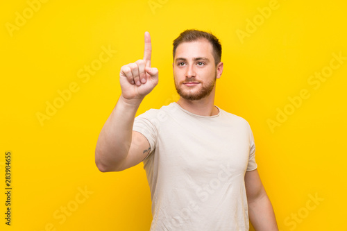 Handsome man over yellow background touching on transparent screen