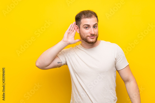 Handsome man over yellow background listening something