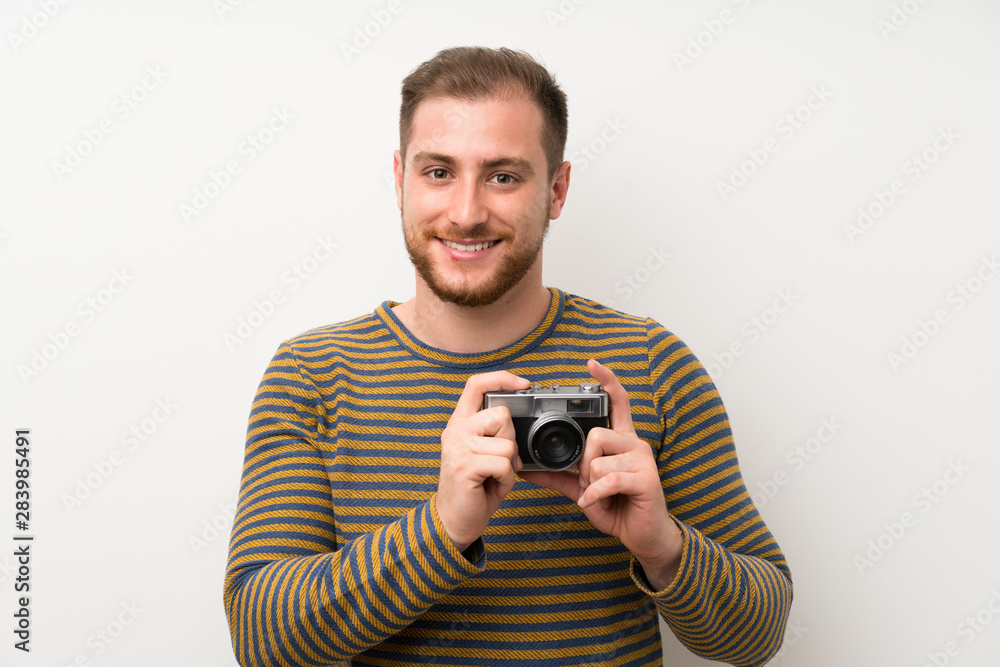Handsome man over isolated white wall holding a camera Handsome man over isolated white wall holding a camera