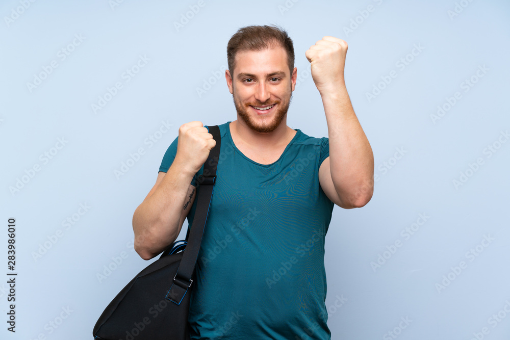 Blonde sport man over blue wall celebrating a victory Blonde sport man over blue wall celebrating a victory