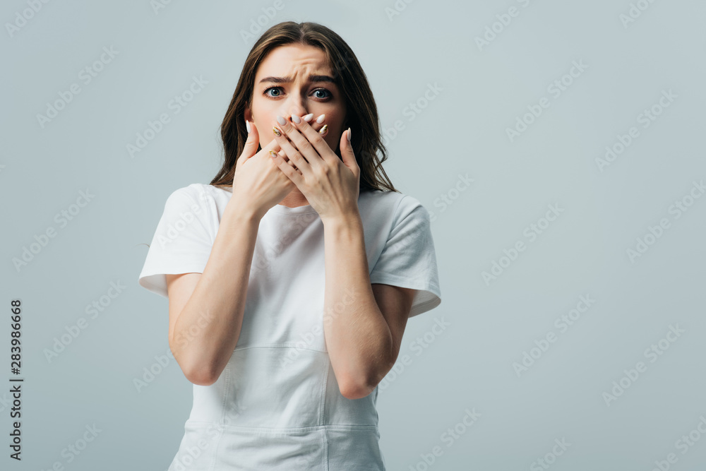 scared beautiful girl in white t-shirt covering mouth with hands isolated on grey scared beautiful girl in white t-shirt covering mouth with hands isolated on grey
