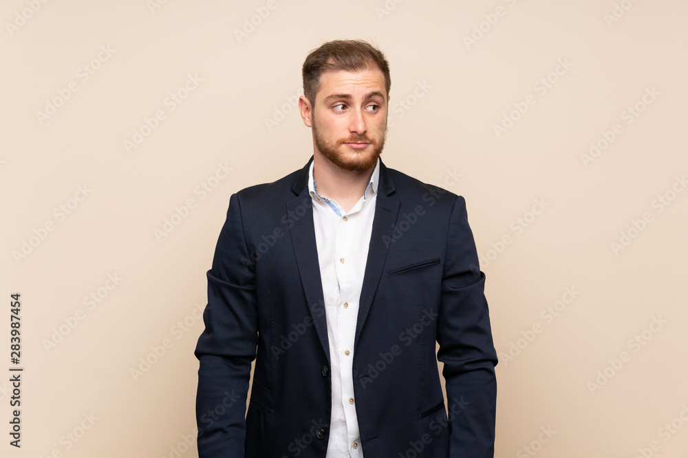 Blonde man over isolated background making doubts gesture looking side Blonde man over isolated background making doubts gesture looking side