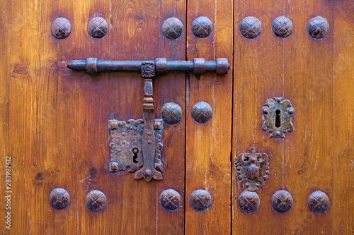 Very old ornamental wooden door locked with a bolt and vintage locks.