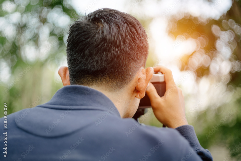 Rear view of a professional male photographer holding vintage film camera to take photo in the evening sunset Rear view of a professional male photographer holding vintage film camera to take photo in the evening sunset