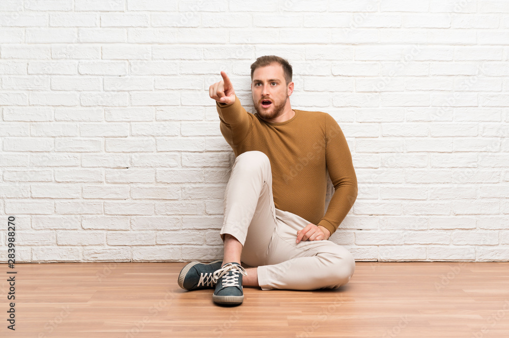 Blonde man sitting on the floor pointing away Blonde man sitting on the floor pointing away