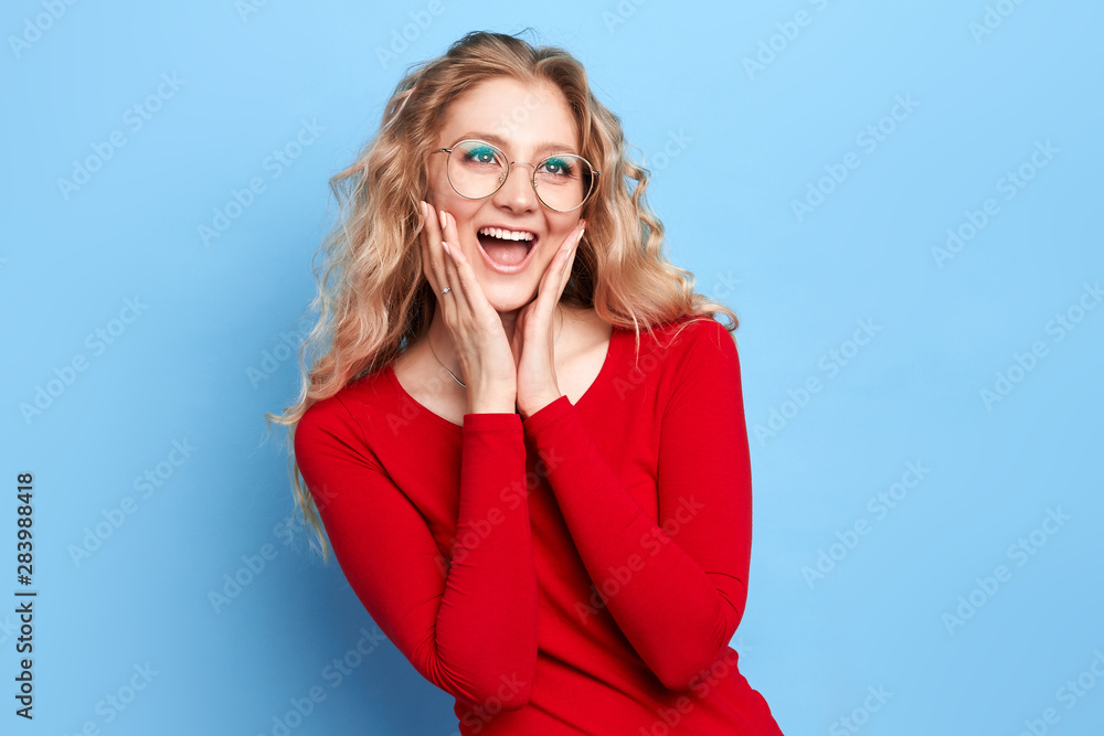 Crazy sale, discounts Portrait of stylish positive cheerful girl with long fair wavy hair in casual clothes , opened mouth, palms holding cheeks,looking up isolated over blue. close up portrait Crazy sale, discounts Portrait of stylish positive cheerful girl with long fair wavy hair in casual clothes , opened mouth, palms holding cheeks,looking up isolated over blue. close up portrait