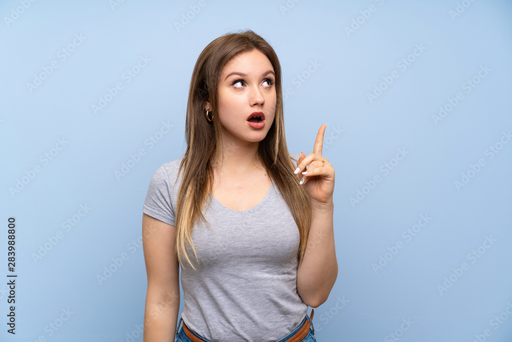 Teenager girl over isolated blue wall thinking an idea pointing the finger up Teenager girl over isolated blue wall thinking an idea pointing the finger up