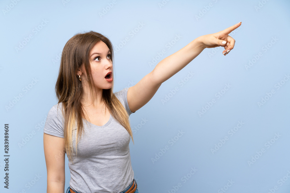 Fototapeta premium Teenager girl over isolated blue wall pointing away