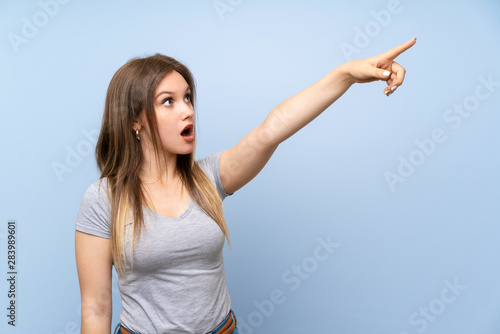 Teenager girl over isolated blue wall pointing away