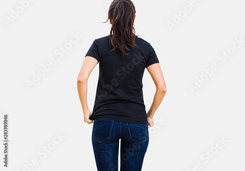 Back view of slender brunette woman adjusting black T shirt over denim jeans