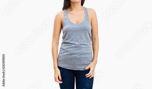 Slender brunette woman in heathered gray tank top and denim jeans isolated on light gray background photo