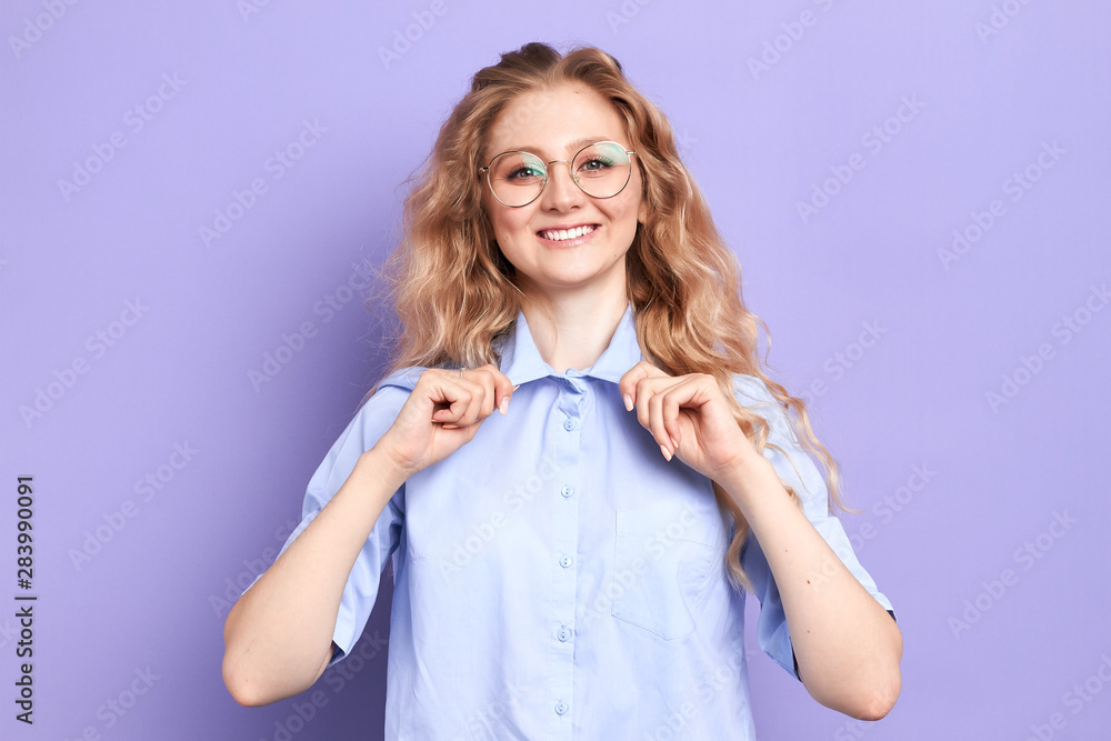 smiling happy woman in glasses touching her shirt collar. isolated blue background, emotion and feeling, happiness, woman rejoicing at the new work in the office smiling happy woman in glasses touching her shirt collar. isolated blue background, emotion and feeling, happiness, woman rejoicing at the new work in the office