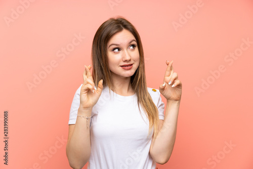 Teenager girl over isolated pink wall with fingers crossing © luismolinero