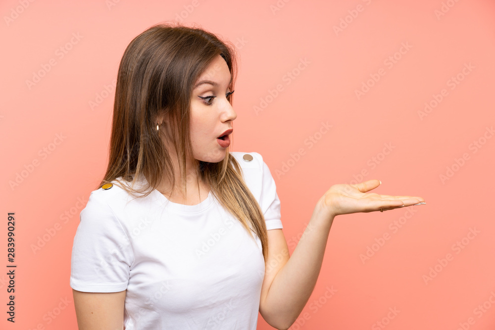 Teenager girl over isolated pink wall holding copyspace imaginary on the palm Teenager girl over isolated pink wall holding copyspace imaginary on the palm