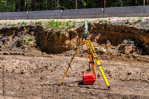 Surveyor engineer with equipment (theodolite or total positioning station) on the construction site of the road, highway or building in background