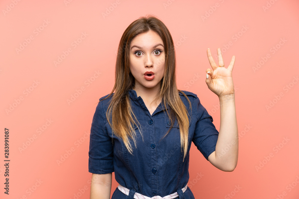 Teenager girl over isolated pink background surprised and showing ok sign Teenager girl over isolated pink background surprised and showing ok sign