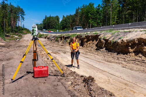 Surveyor engineer with equipment (theodolite or total positioning station) on the construction site of the road, highway or building in background