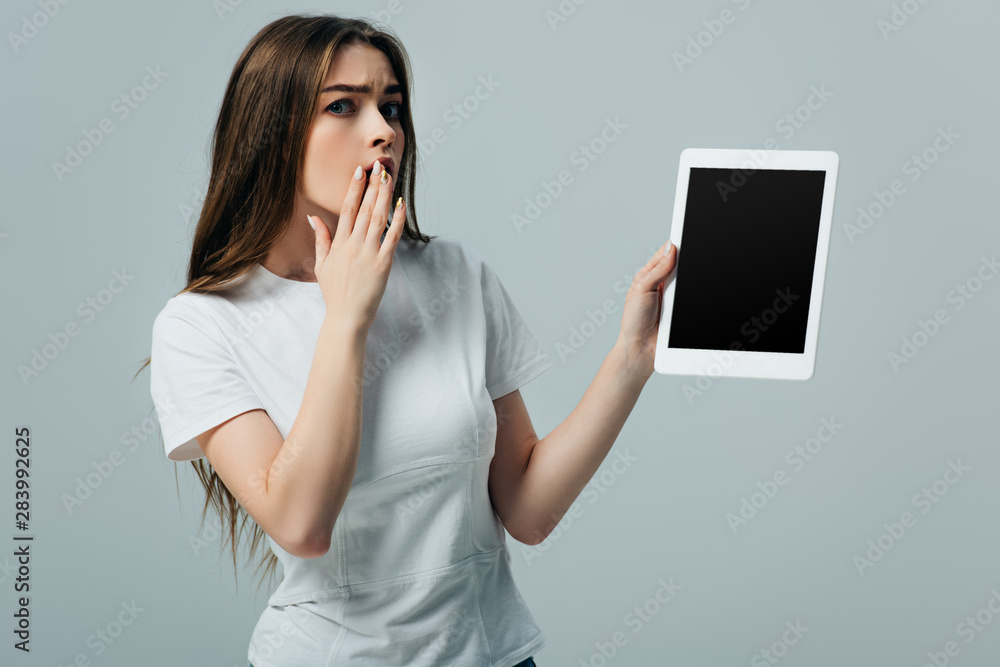 shocked beautiful girl in white t-shirt showing digital tablet with blank screen isolated on grey shocked beautiful girl in white t-shirt showing digital tablet with blank screen isolated on grey