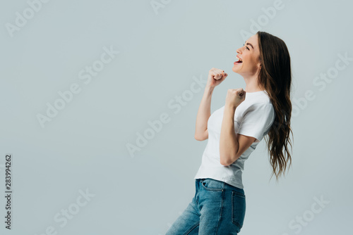 side view of happy beautiful girl in white t-shirt showing yes gesture isolated on grey