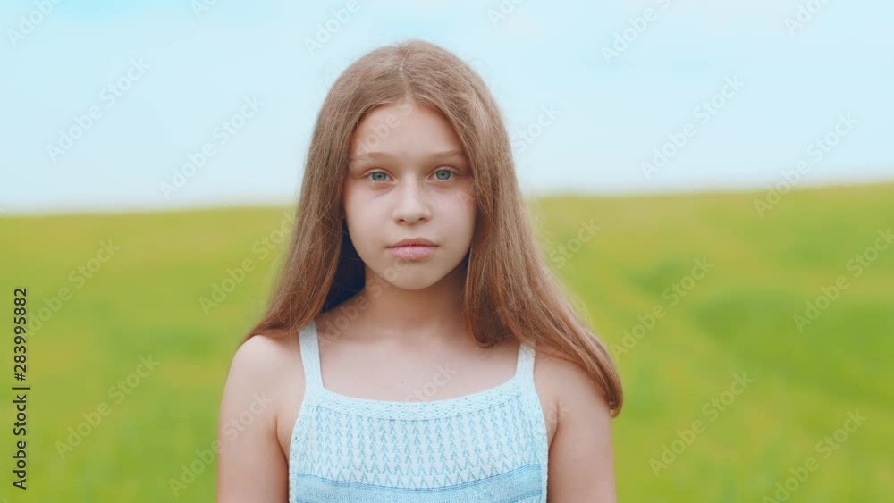 Close up view of adorable sweet blue-eyed little girl in white dress looking straight to camera and smiling happily on blurred green meadow background. Childhood, nature lover, portrait Close up view of adorable sweet blue-eyed little girl in white dress looking straight to camera and smiling happily on blurred green meadow background. Childhood, nature lover, portrait
