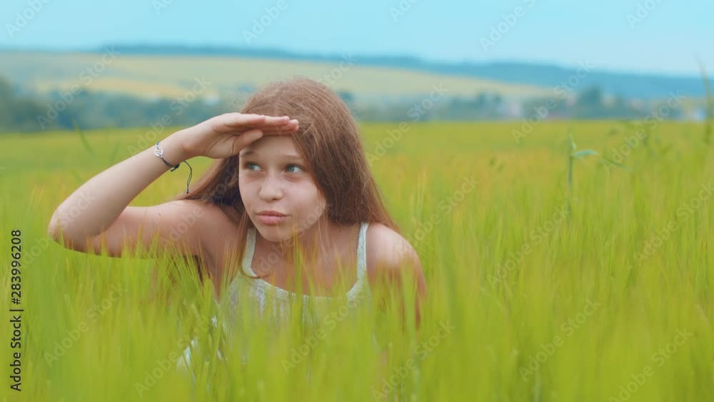 Close up view of cheerful little girl playing hide-and-seek in high-grass, covers her eyes with her palm and looking around. Happy childhood, positive emotions, good mood. Happiness concept Close up view of cheerful little girl playing hide-and-seek in high-grass, covers her eyes with her palm and looking around. Happy childhood, positive emotions, good mood. Happiness concept