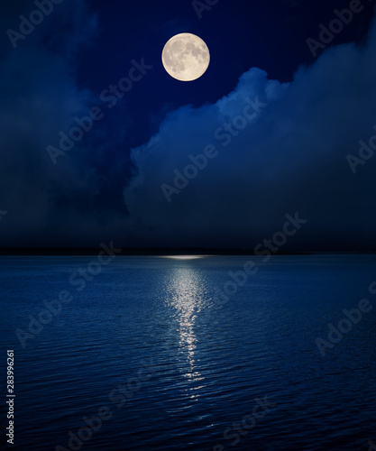 full moon in dark sky over clouds and water in river