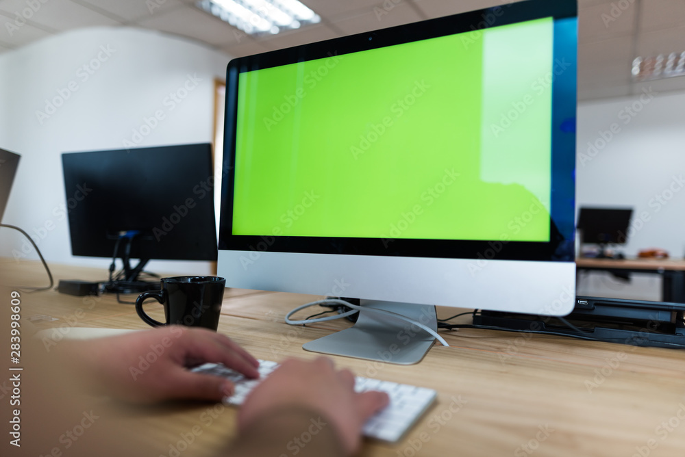 Hombre frente a pantalla de computador escribiendo en pantalla verde, con teclado y mouse junto a un café y más pantallas Hombre frente a pantalla de computador escribiendo en pantalla verde, con teclado y mouse junto a un café y más pantallas