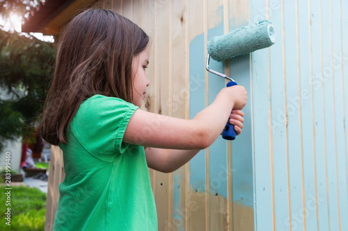 Young girl painting little wooden house with a roller