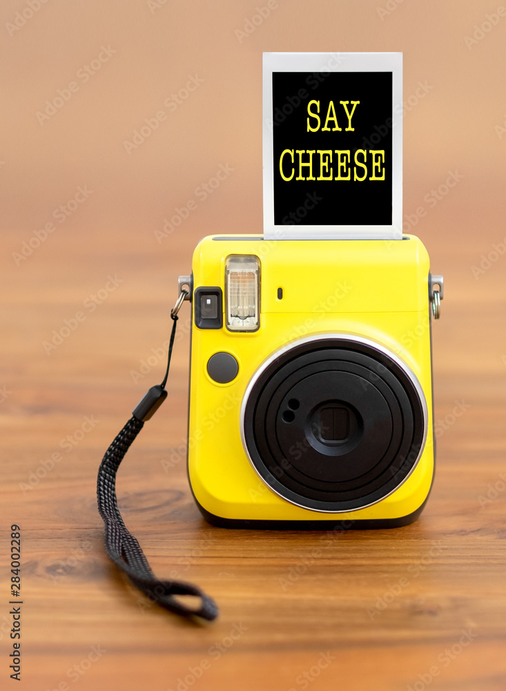 Bright yellow instant camera with photo that reads "say cheese". Wooden  background. Shallow depth of field. Stock Photo | Adobe Stock