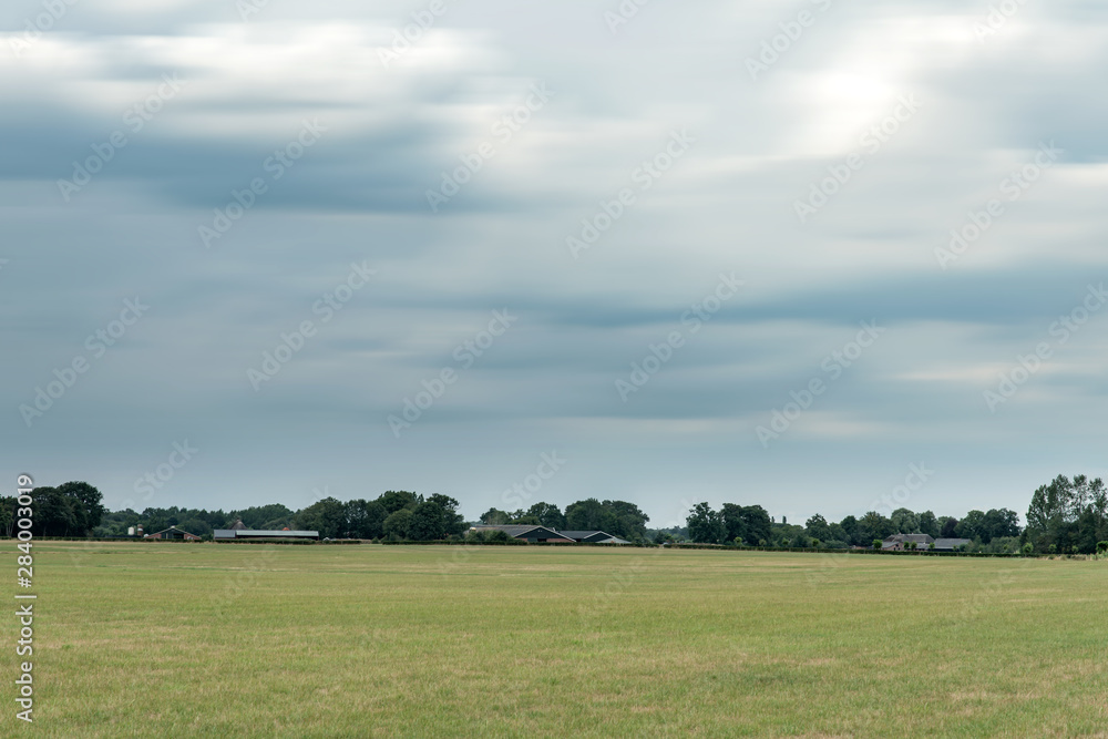 Meadow with forest on horizon under dark cloudy sky. Long exposure shot.